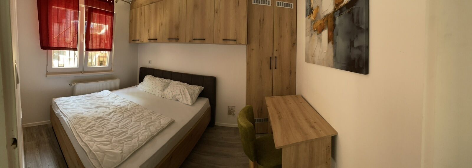 A bedroom with a bed, wooden wardrobe, and a small desk.