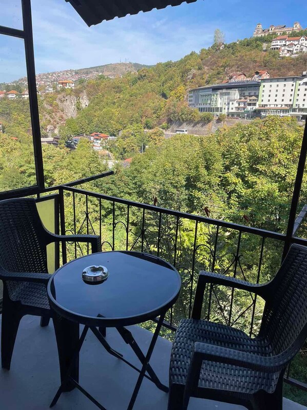 Uma varanda com mesa e cadeiras, com vista para uma encosta com edifícios e vegetação.