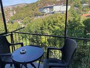 A balcony with a table and chairs, overlooking a hillside with buildings and trees. - The Nest (Sarajevo)