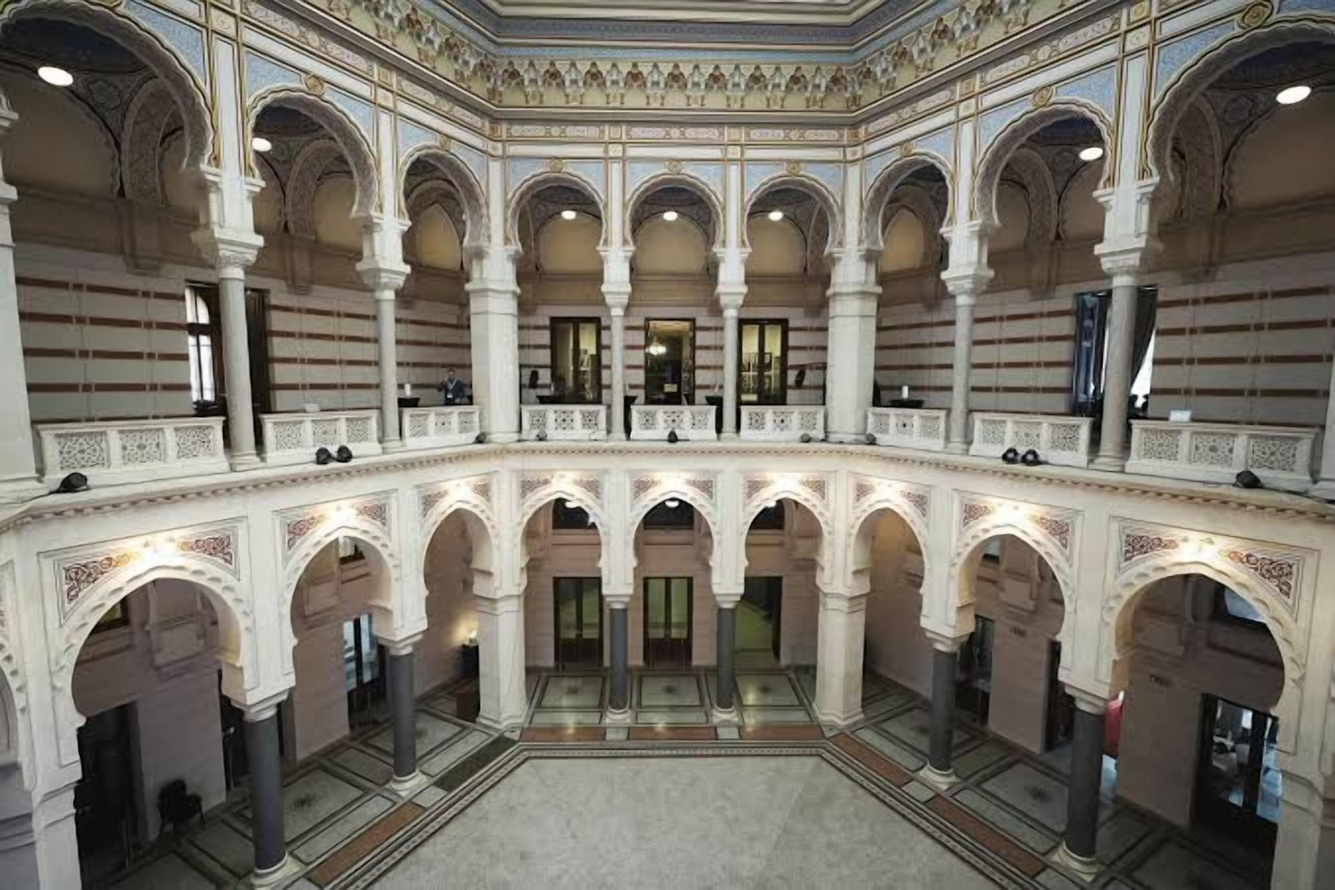 A grand hall with multiple arches and columns, a central open space, and a balcony overlooking the area.