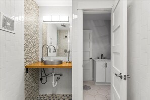 A modern bathroom with a wooden vanity, a sink, and a shower area. - Walkable 2-home Eastside Austin Oasis (Austin)