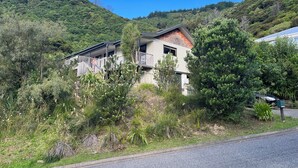 Una casa de dos pisos con balcón, rodeada de exuberante vegetación y colinas.