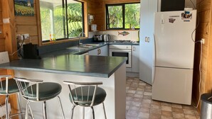 Cocina compacta con una isla central, taburetes de bar, un refrigerador y una ventana con vista a la vegetación.