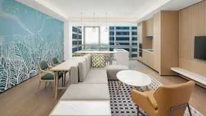 Une chambre d’hôtel moderne dotée d’un coin repas, d’un canapé, d’une table ronde et d’une grande fenêtre donnant sur la ville.
