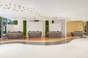 Uma área de recepção moderna com piso curvo, dois balcões de atendimento, jardins verticais verdes e luminárias pendentes.