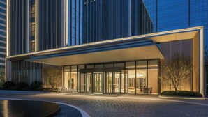 Une entrée d’hôtel moderne avec une façade en verre, un espace d’entrée abrité et une cour aménagée.