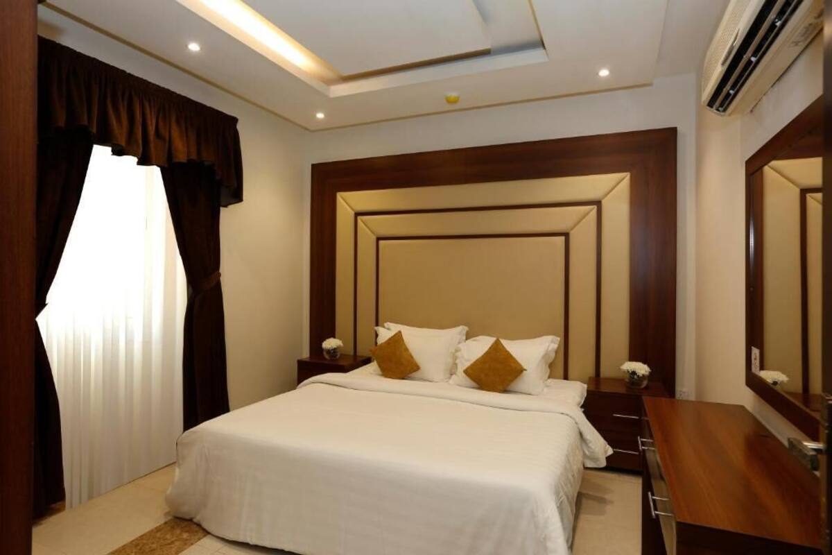 Ein Hotelzimmer mit einem großen Bett, einem Holz-Kopfteil, einem Nachttisch mit Lampe, einem Schminktisch und einem großen Spiegel.