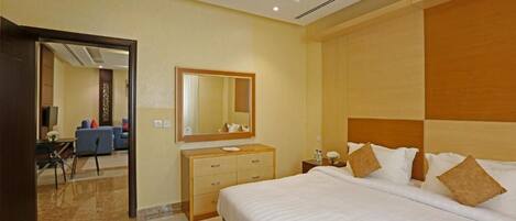 A hotel room with a large bed, a dresser, a mirror, and a view of the living area.