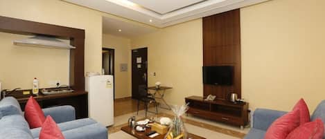 Una sala de estar moderna con un conjunto de sofás, una mesa de centro con objetos, un televisor y una zona de cocina con un refrigerador.