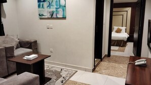 A modern hotel room with a sofa, a small table, a painting on the wall, and a bed with a nightstand. - Hotelier Suites by Cantonal (Riyadh)