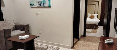 Una habitación de hotel moderna con un sofá, una mesita, un cuadro en la pared y una cama con una mesita de noche.
