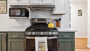 A kitchen with white cabinets, a stainless steel stove, a microwave, and a kettle. - Packer Pilgrimage 1 - Sunroom + Pet Friendly (Green Bay)