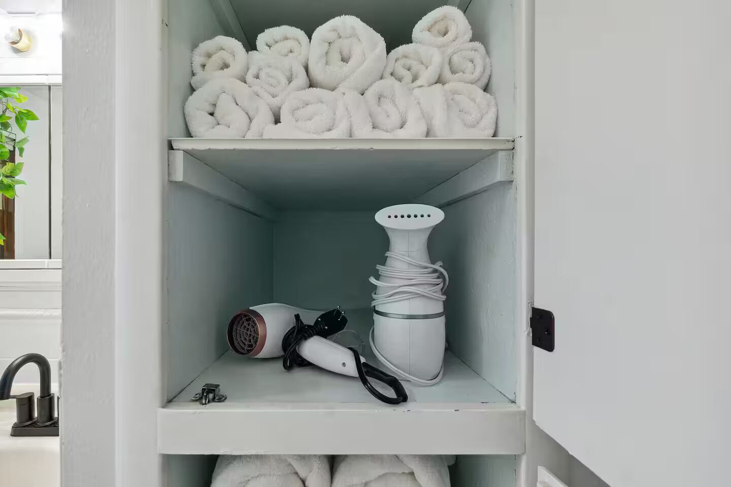 A bathroom with a towel rack holding rolled towels, a hairdryer, and a curling iron on a shelf.