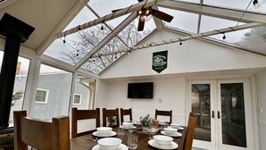 A dining area with a wooden table set for four, a ceiling fan, and a television on the wall. - Packer Pilgrimage 1 - Sunroom + Pet Friendly (Green Bay)