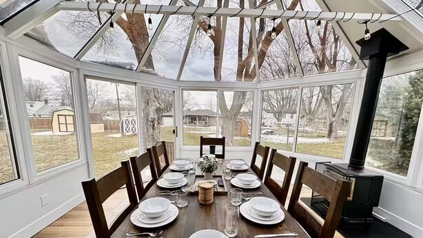 A conservatory with a dining table set for six, surrounded by large windows offering a view of the backyard. - Packer Pilgrimage 1 - Sunroom + Pet Friendly (Green Bay)