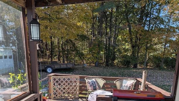 An outdoor deck with a grill, seating area, and a view of a wooded area.