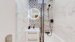 Bathroom features a round mirror, sink, and handheld showerhead.
