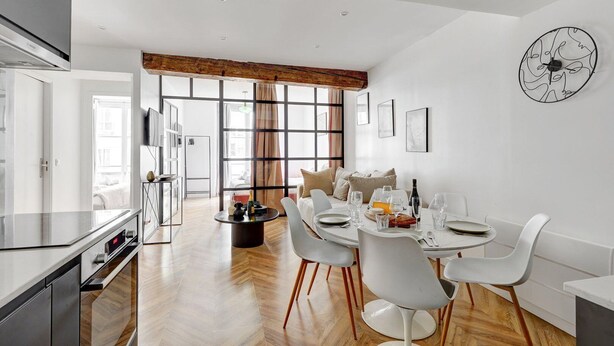 Un espace repas moderne avec une table ronde, des chaises blanches et une horloge au mur.