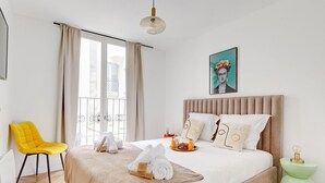 Une chambre d’hôtel moderne avec un grand lit, un fauteuil jaune et une vue sur la ville par la fenêtre.
