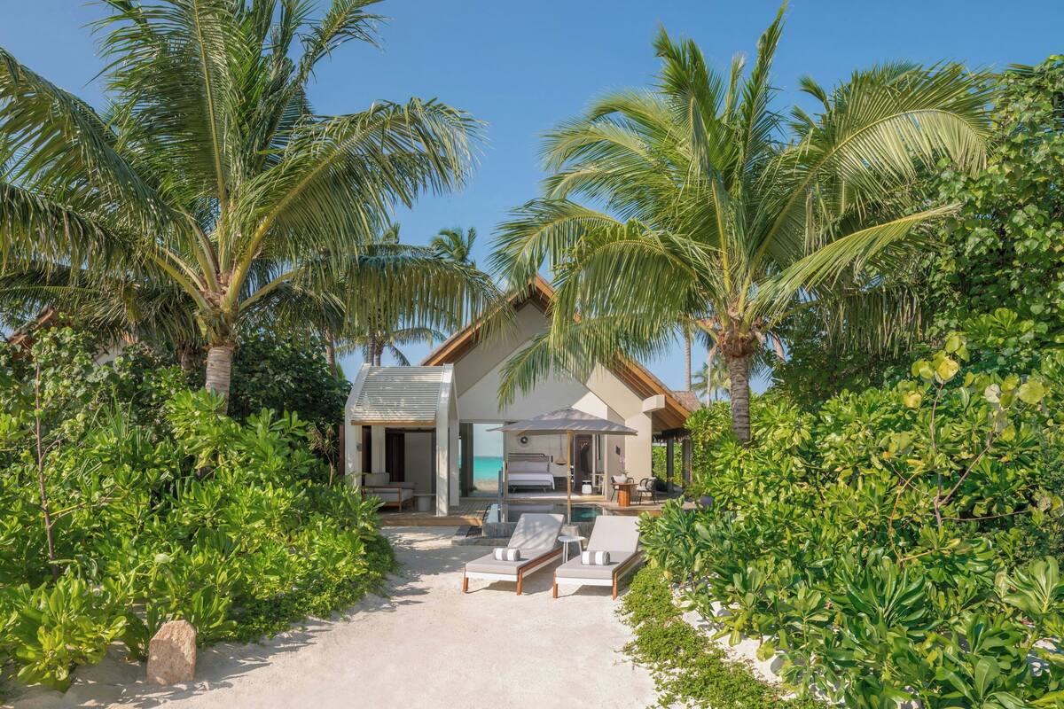 A beachfront property with a pool, lounge chairs, and palm trees.