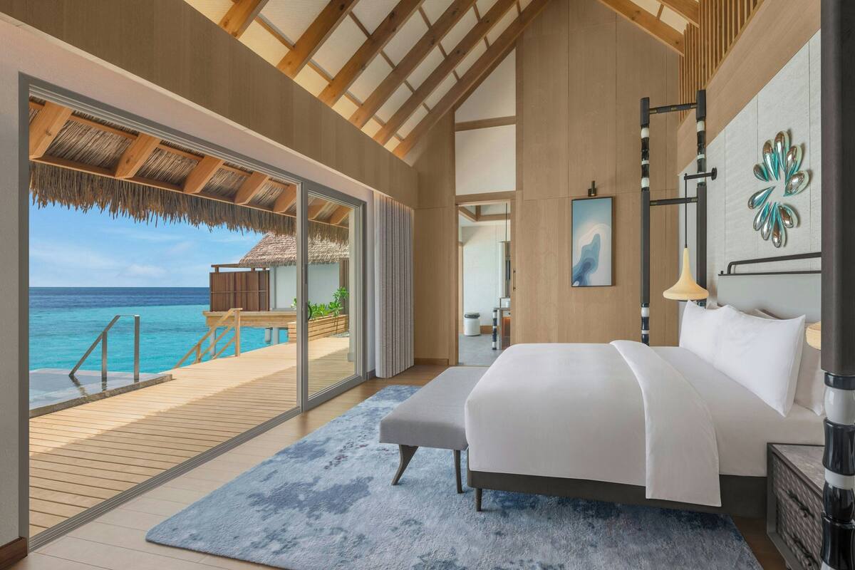 A modern bedroom with a large bed, a view of the ocean, and a wooden ceiling.
