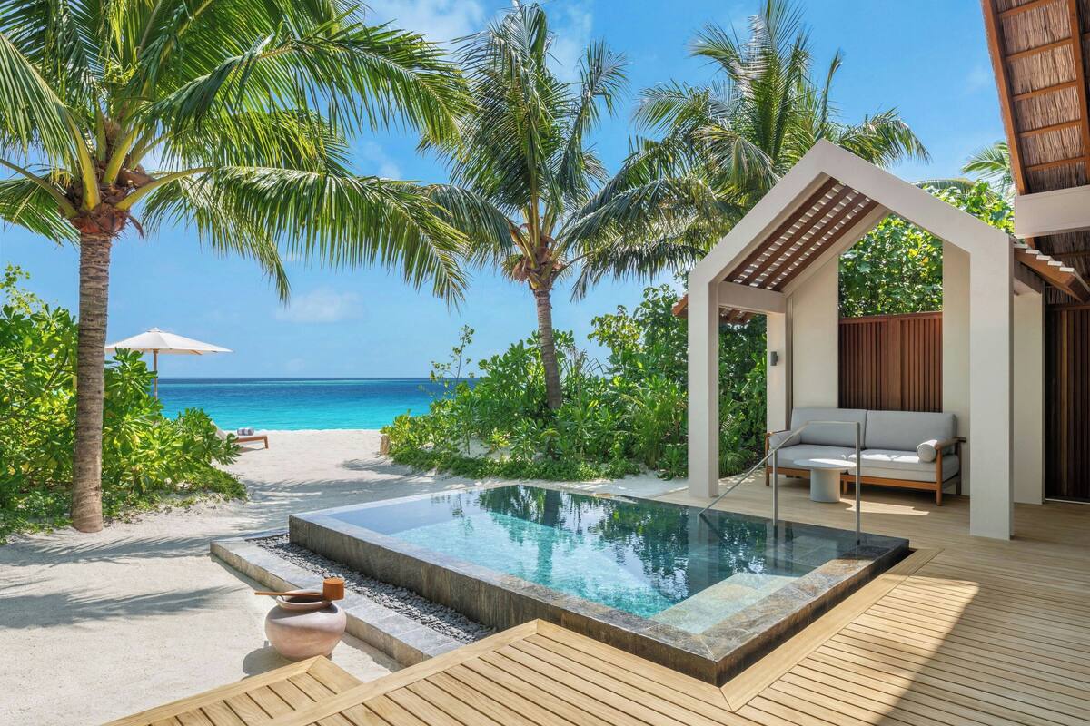 A pool area with a view of the ocean, surrounded by palm trees and a wooden deck.