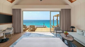 A hotel room with a large bed, a TV, a desk, a chair, a sofa, and a balcony with a view of the ocean. - JW Marriott Maldives Kaafu Atoll Island Resort (Hathaa Finolhu)