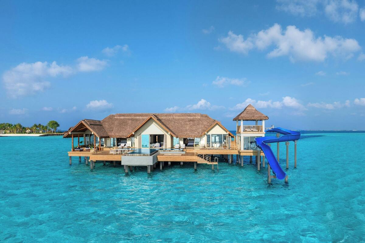 Overwater bungalows with thatched roofs, a blue slide, and clear turquoise water.
