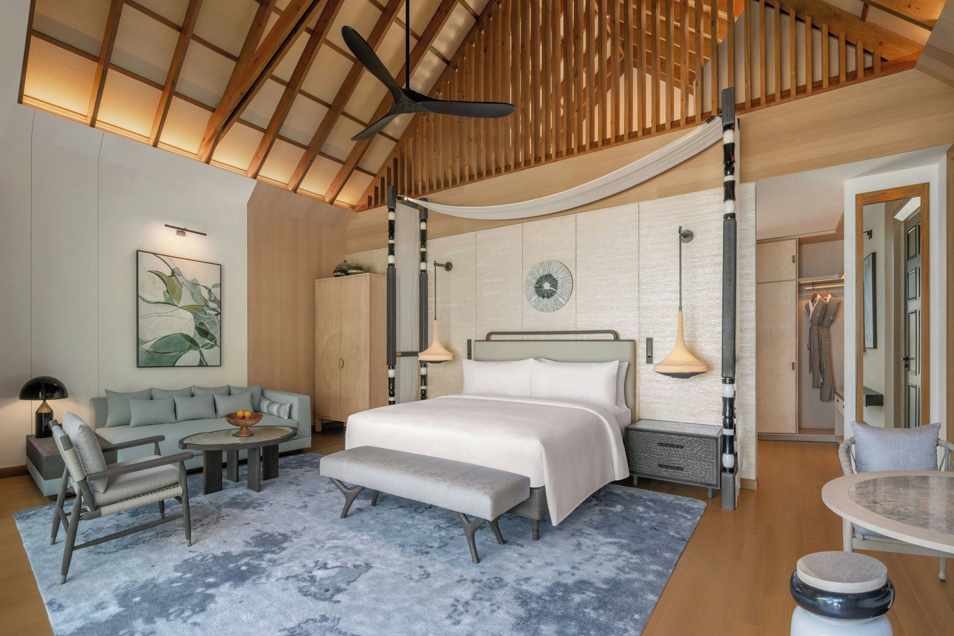 Une chambre d’hôtel moderne dotée d’un grand lit, d’un coin salon avec un canapé et des fauteuils, d’une table à manger et d’un ventilateur de plafond.