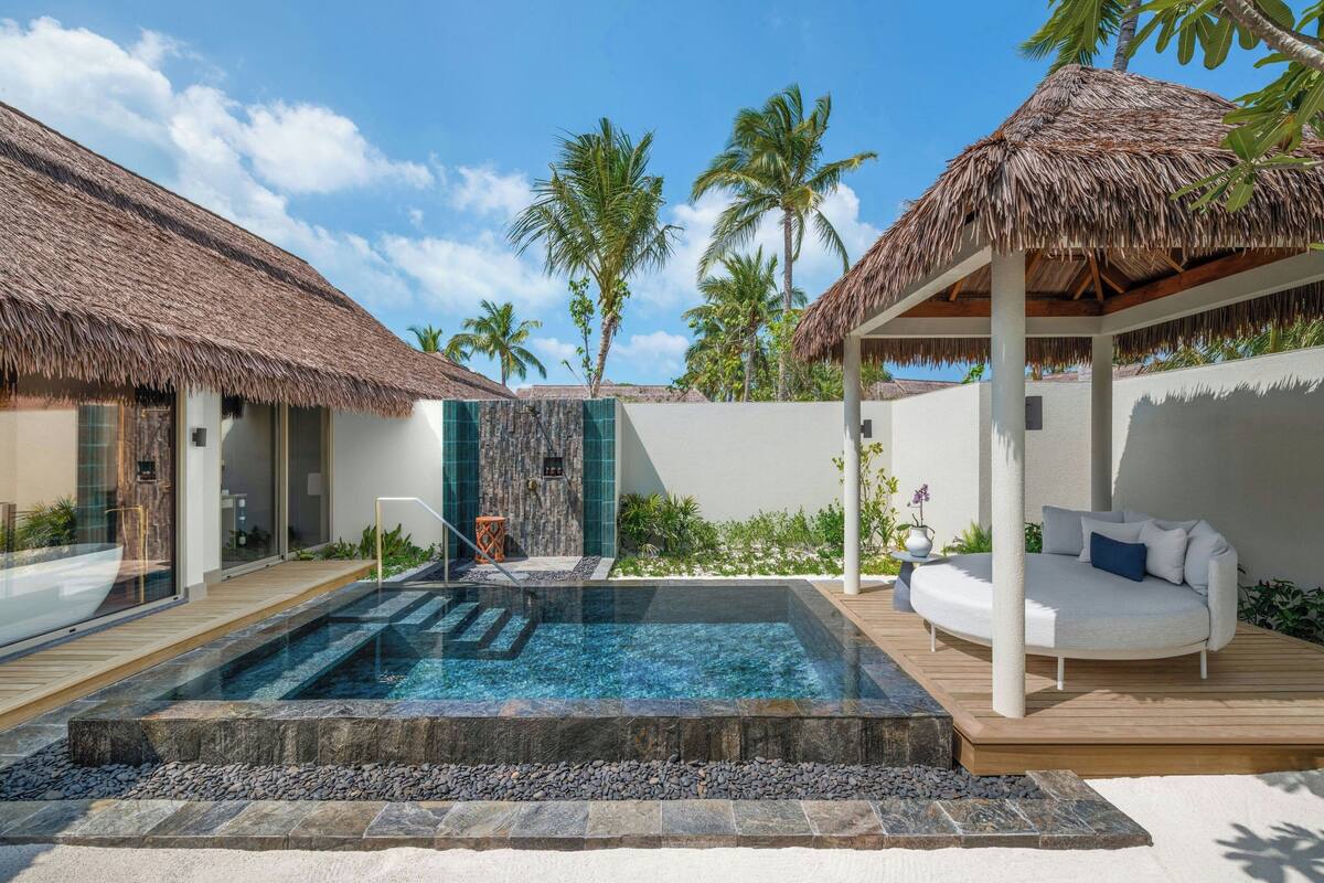 A pool area with a hot tub, a thatched-roof structure, and a white outdoor sofa.