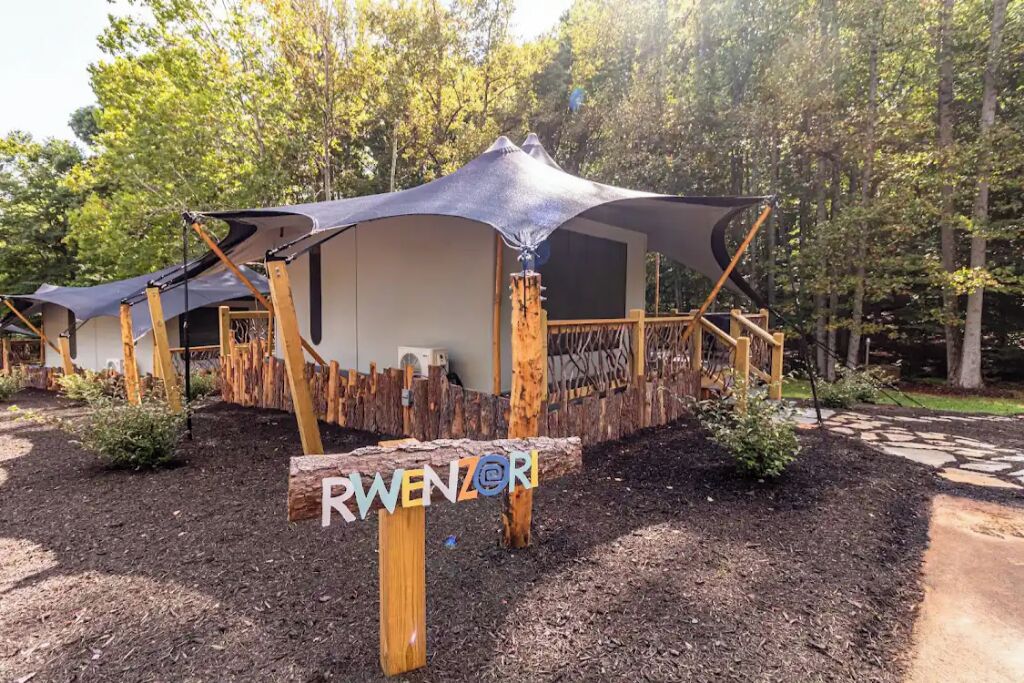 A series of wooden yurts with attached canopies, surrounded by a wooden fence and a sign that reads "RWENZOR".