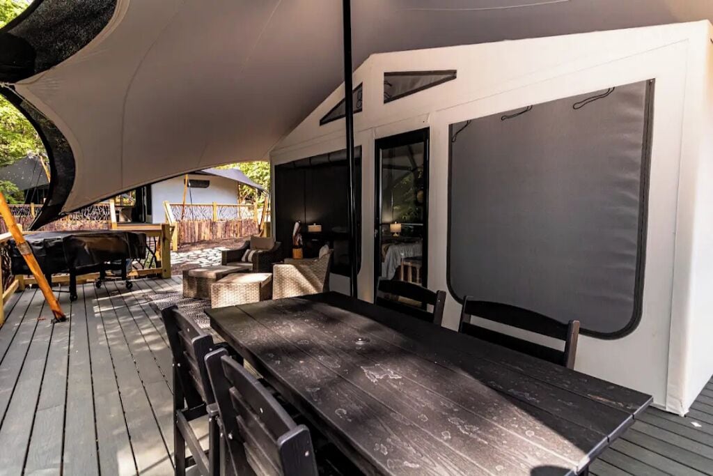 An outdoor deck with a wooden table and chairs, a covered seating area, and a large window.