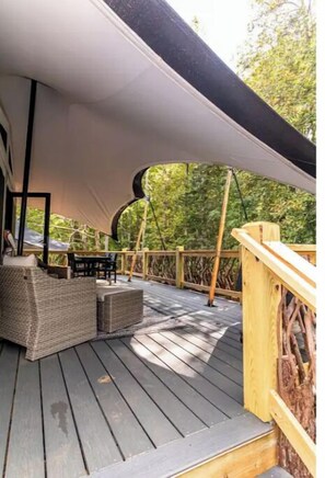 A covered outdoor deck with wicker furniture and a wooden railing. - RWENZORI, a Unique Luxury Tent Experience, at Karoo Smith Mountain Lake  (Wirtz)