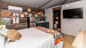 A bedroom with a bed, a TV, a kitchen area, and a bathroom.