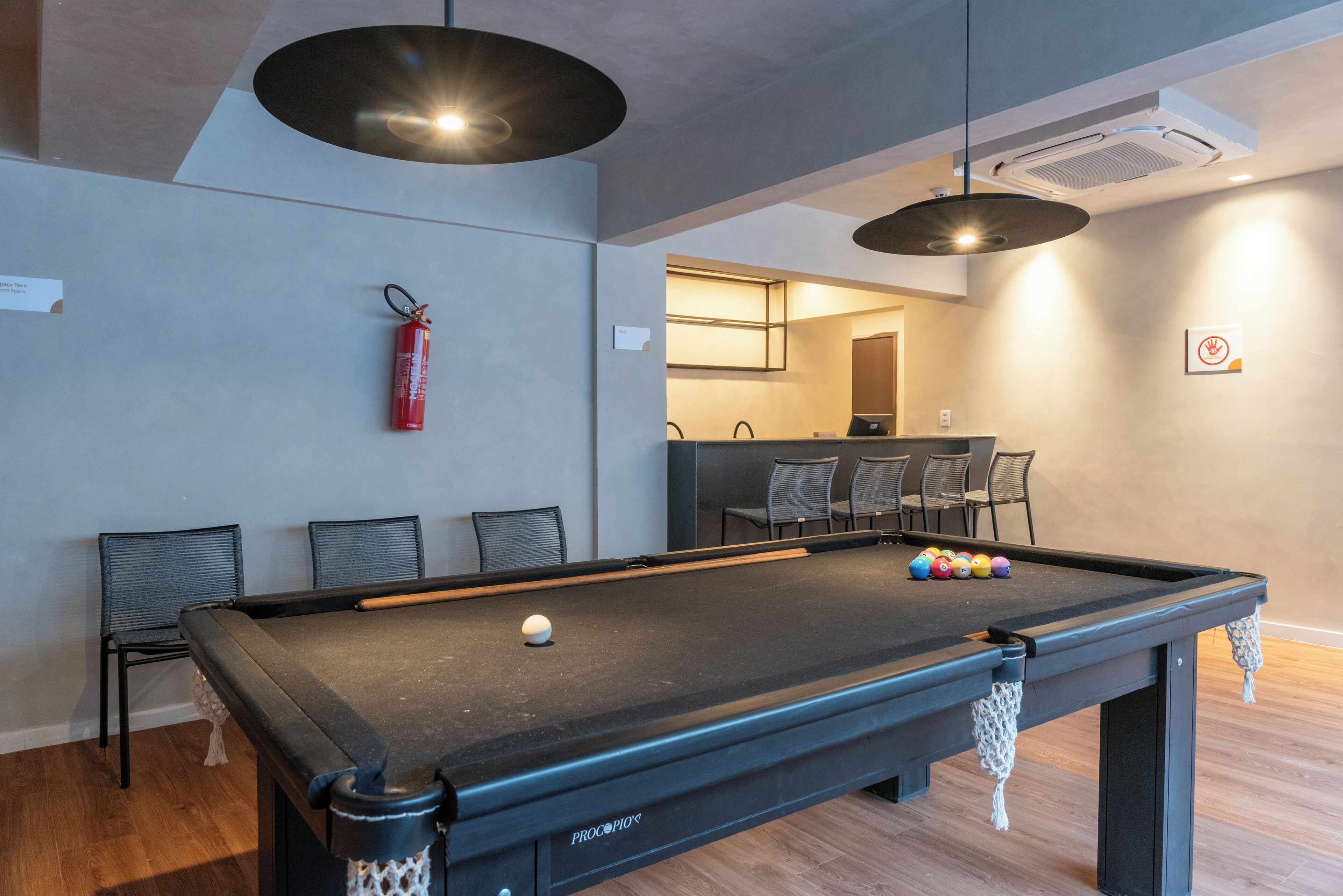 A pool table with a fire extinguisher, chairs, and a bar area in the background.