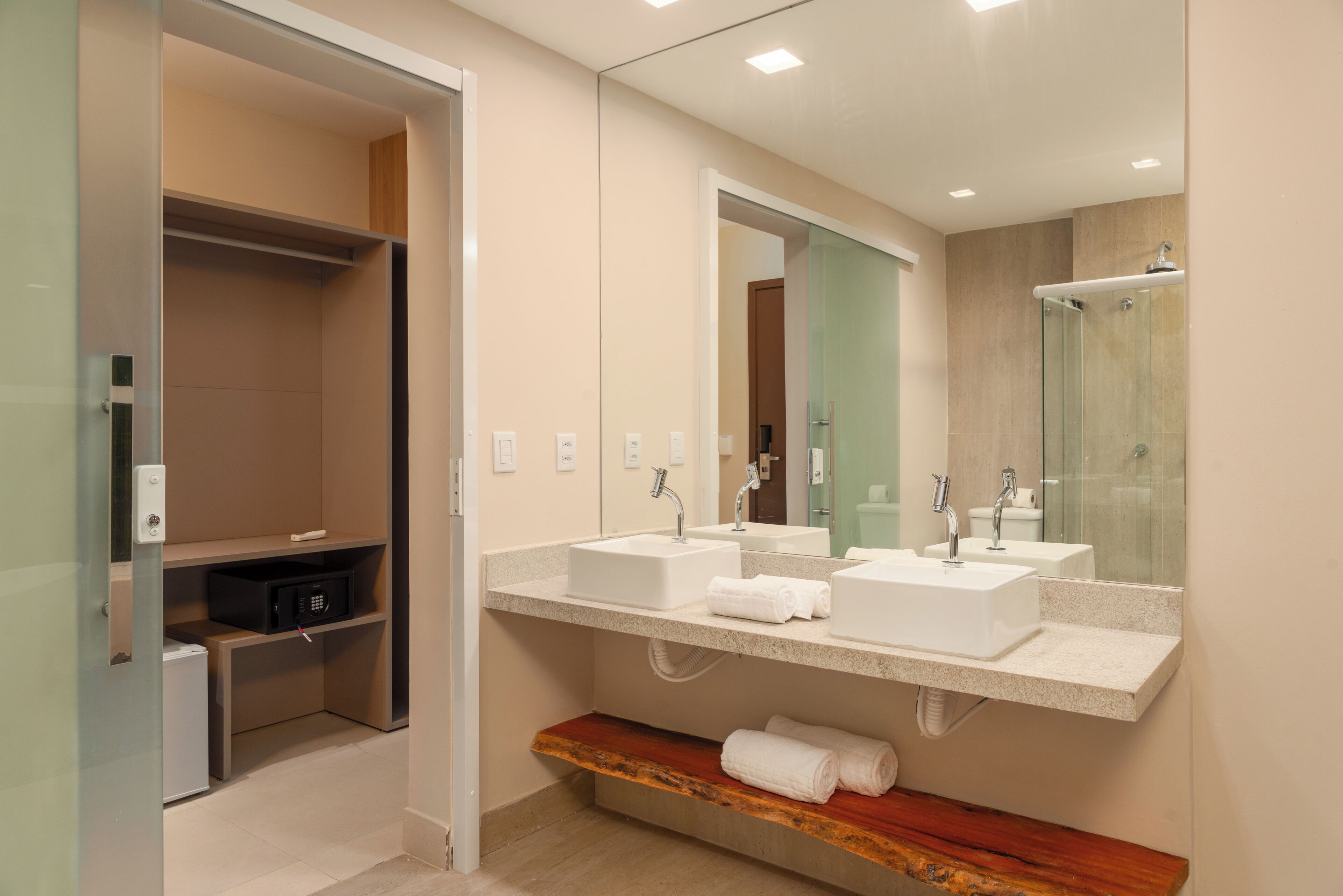A modern bathroom with two sinks, a glass shower enclosure, and a wooden shelf with towels.