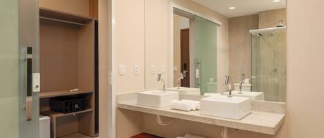 A modern bathroom with two sinks, a glass shower enclosure, and a wooden shelf with towels.