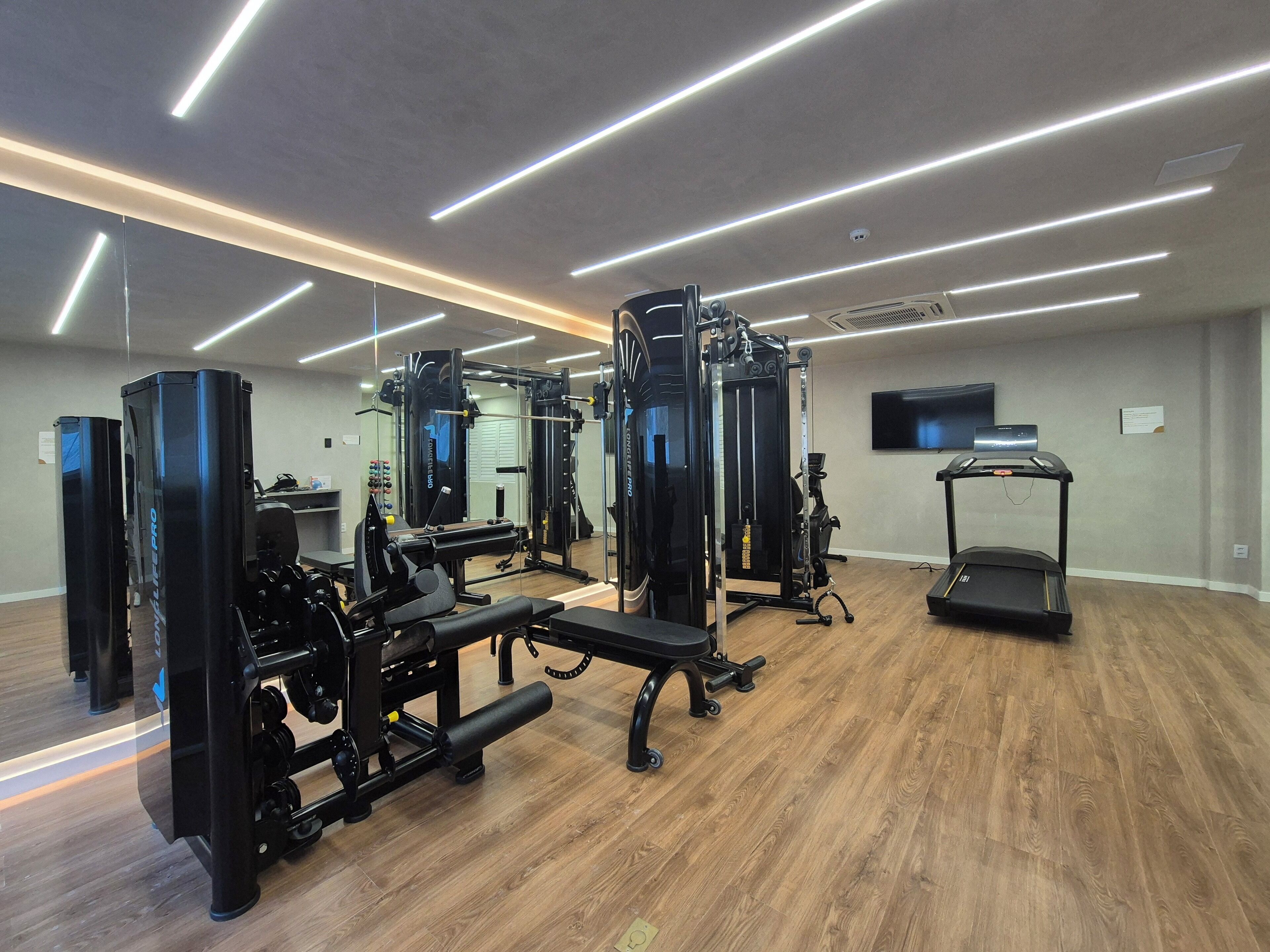 Ein modernes Fitnessstudio mit unterschiedlichen Trainingsgeräten, einem Laufband und einem an der Wand befestigten Fernseher.