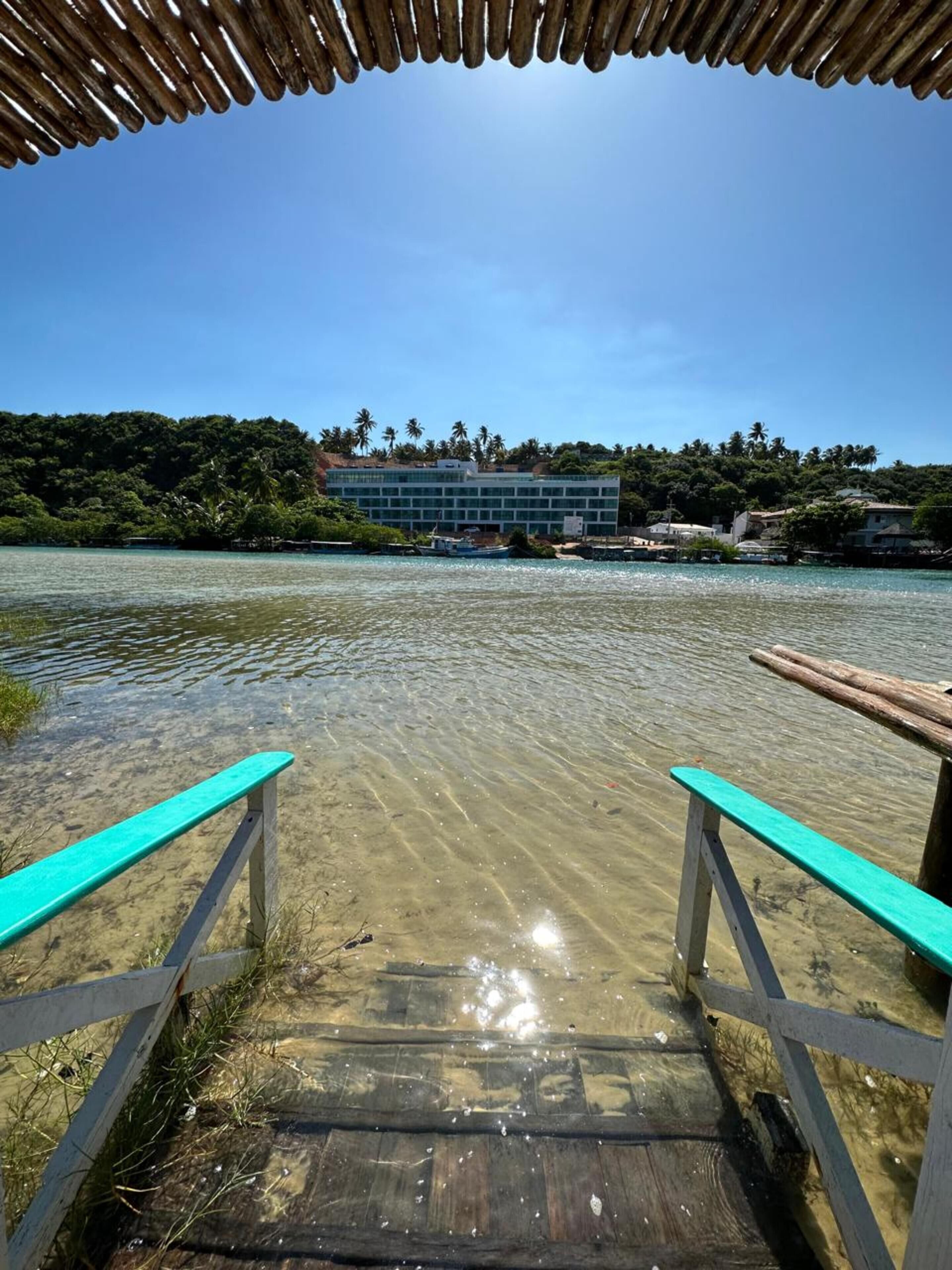 A wooden dock leading to a clear water body with a building in the background.