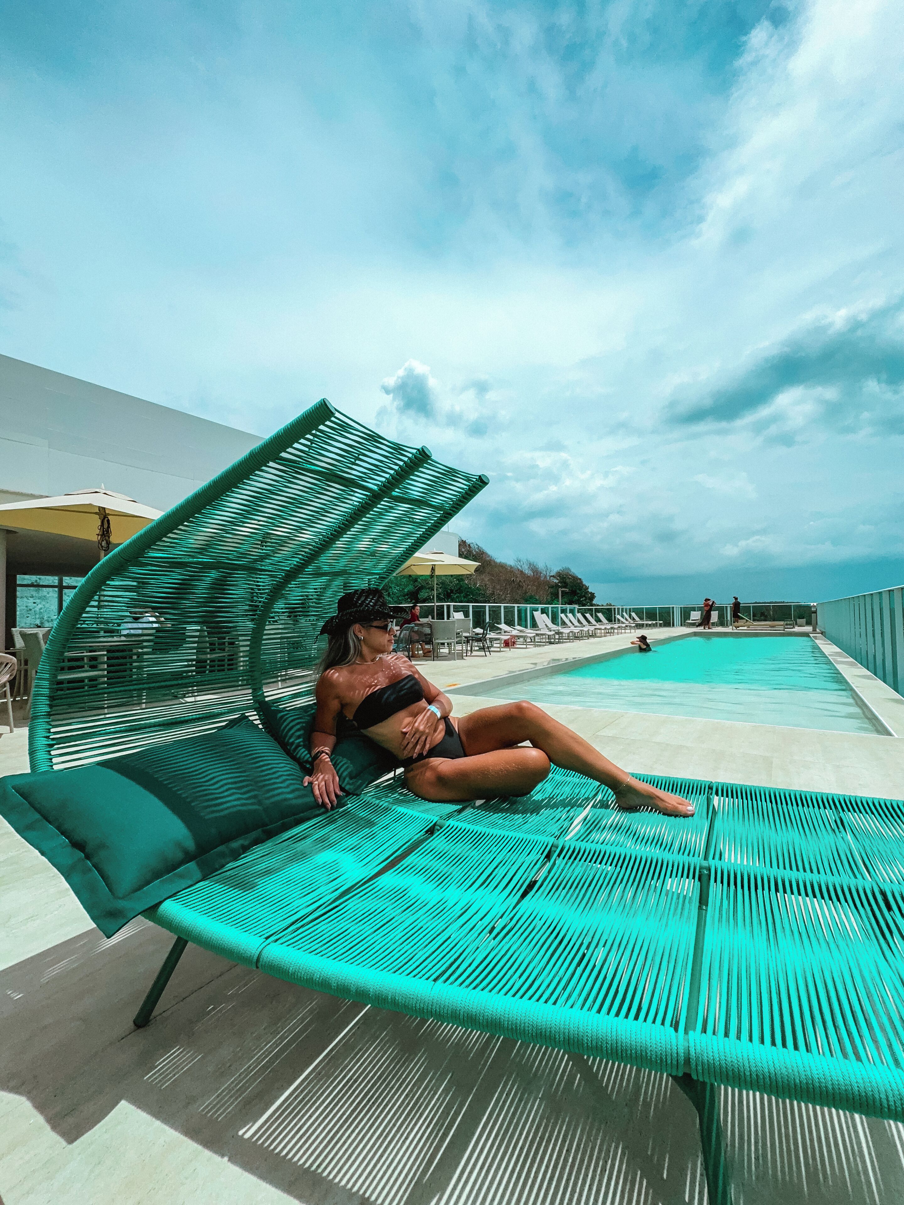 Une personne se détend sur un fauteuil de jardin vert, près d'une piscine.
