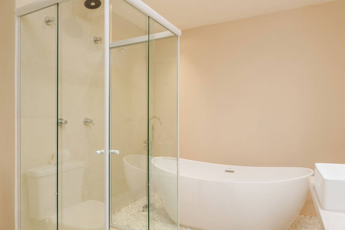 Un baño moderno con ducha envuelta en vidrio, una bañera independiente y un inodoro blanco.