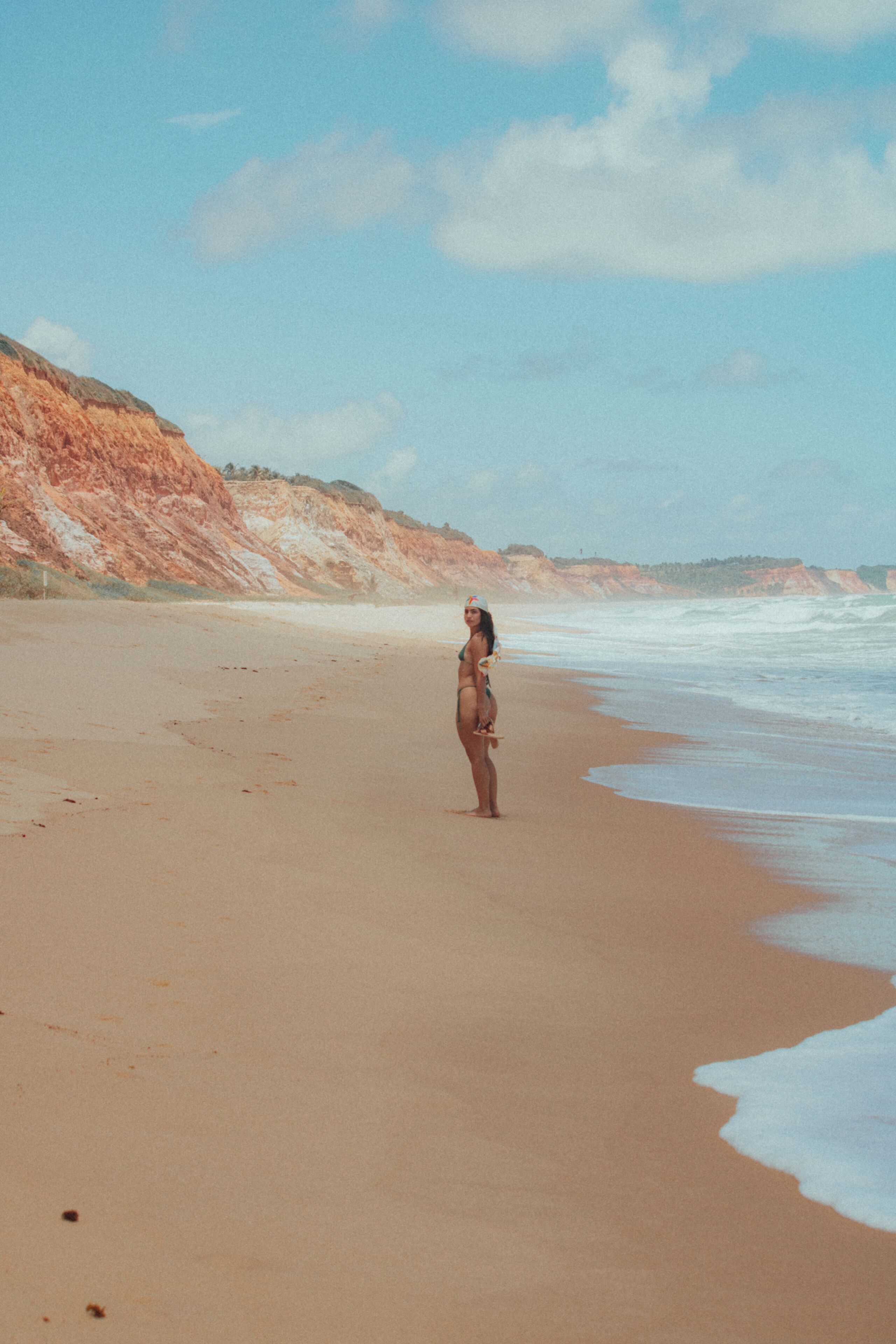 Ein Strand mit einer Person, die auf dem Sand steht, Klippen im Hintergrund und Wellen, die an das Ufer rollen.