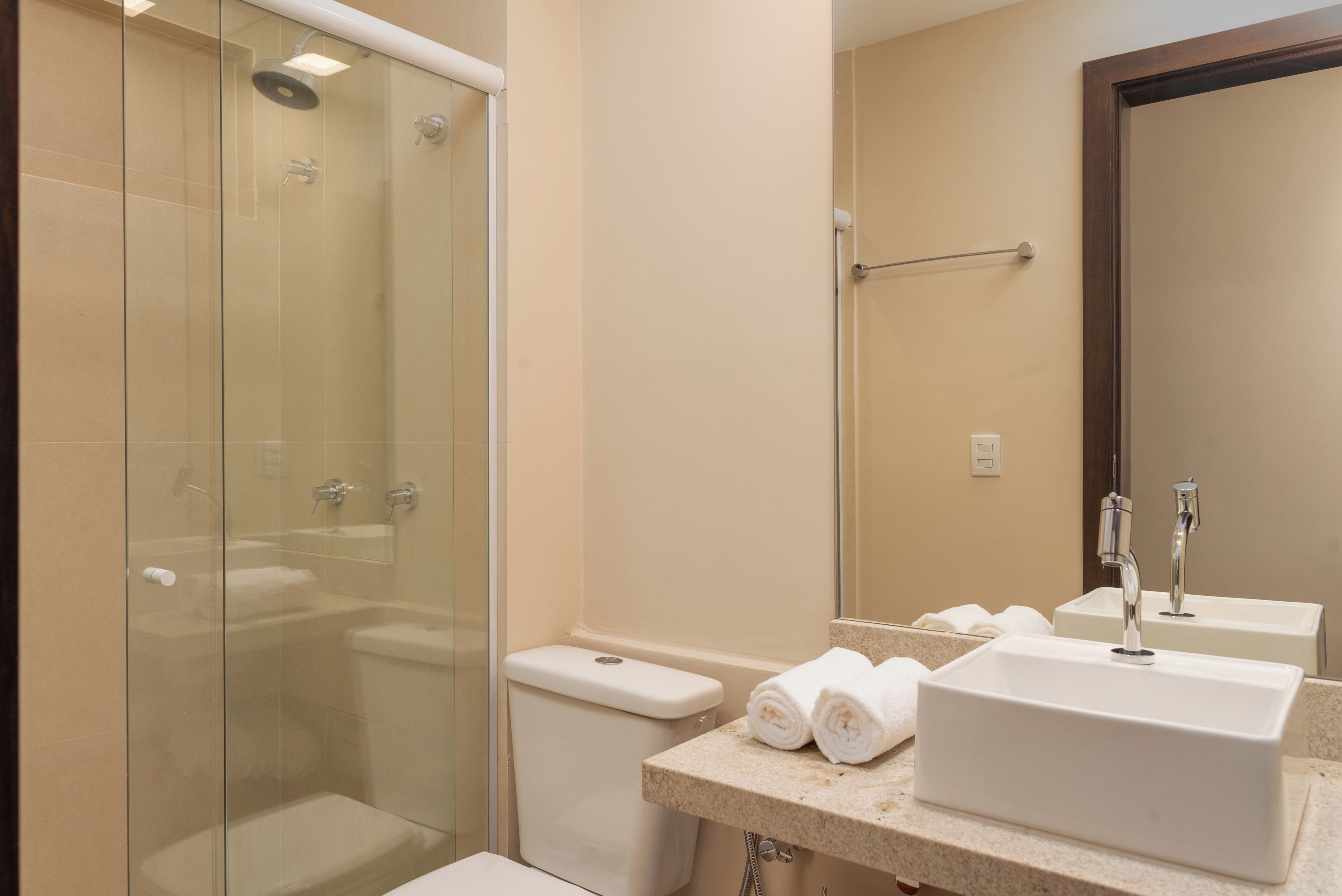 Een moderne badkamer met een douchecabine van glas, een toilet en een wastafelgedeelte met handdoeken.