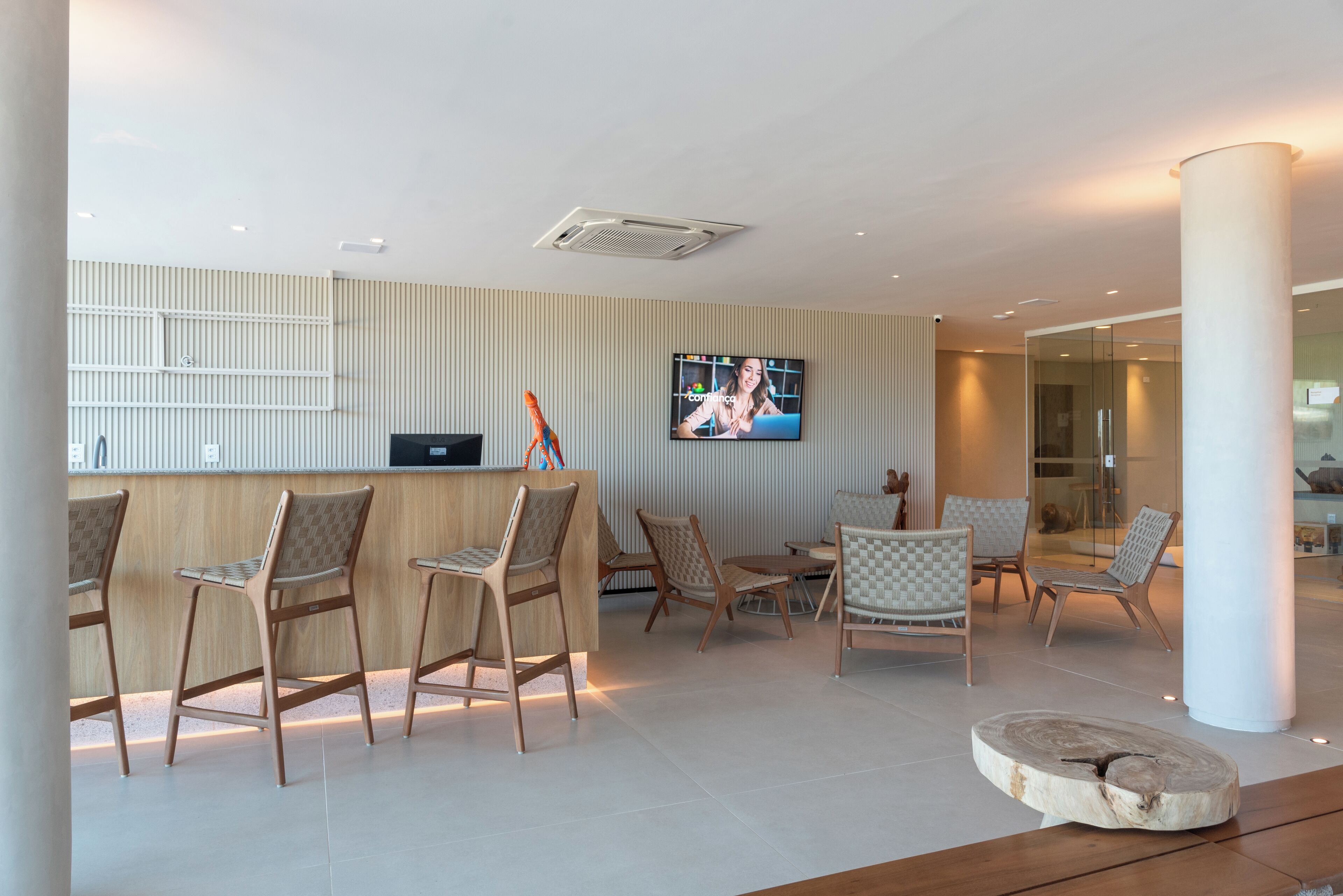 A modern reception area with a TV screen, wooden chairs, and a reception desk.