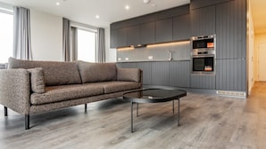 A modern kitchen with grey cabinets, a built-in oven, and a round black coffee table. - London East Village Apartment With City Views (London)