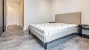 A bedroom with a bed, a nightstand, a headboard, and a wooden floor. - London East Village Apartment With City Views (London)