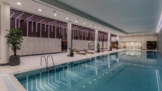 A modern indoor swimming pool with a geometric light pattern on the ceiling, lounge chairs, and potted plants. - London East Village Apartment With City Views (London)