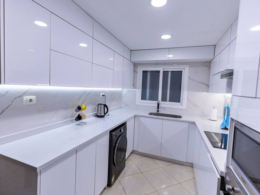 Una cocina moderna con armarios blancos, lavavajillas integrado, una ventana y una campana extractora de acero inoxidable.