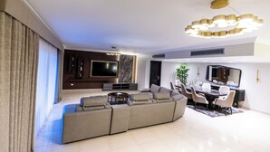 A modern living room with a sectional sofa, a dining table with chairs, a flat-screen TV, and a decorative ceiling light fixture. - Ocean Apartments (Cairo)