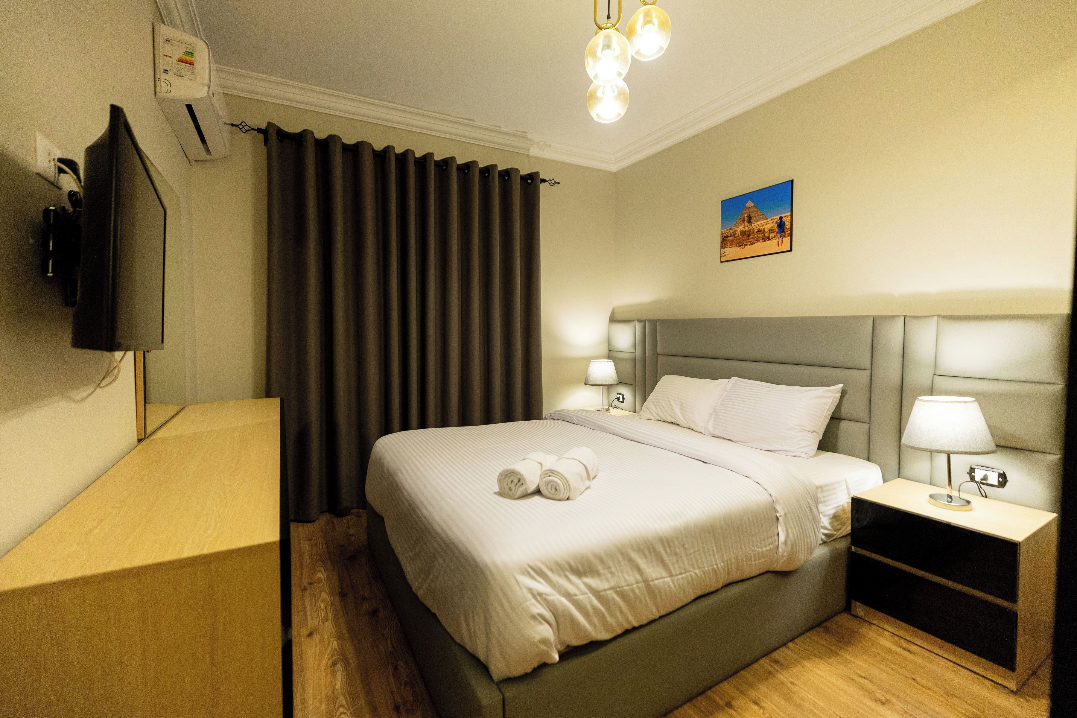 A neatly made bed with a headboard, two bedside lamps, and a wall-mounted TV.